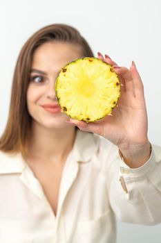 A young attractive pretty nice caucasian smiling woman holds ring slice pineapple covering her eye against a white background. Healthy eating concept