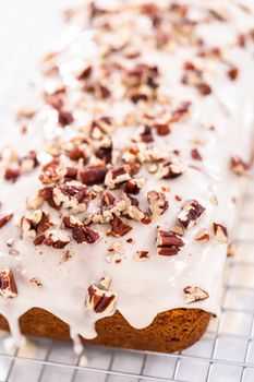 Glazing pumpkin bread with a white glaze and garnishing with shopped pecans.