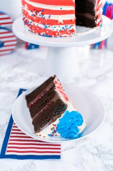 Slice of July 4th chocolate cake decorated with red, white, and blue buttercream frosting on a white plate.