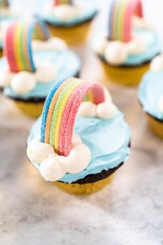 Chocolate cupcakes decorated with blue buttercream frosting and rainbow for unicorn theme birthday party.