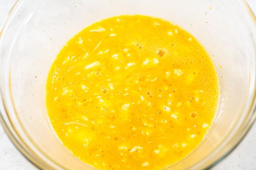 Mixing ingredients with a hand whisk in a glass mixing bowl to make egg bites.