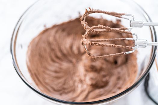 Mixing store-bought chocolate frosting in a mixing glass bowl with a hand mixer.