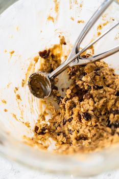 Scooping cookie dough with dough scoop into a baking sheet lined with parchment paper to bake soft oatmeal raisin walnut cookies.