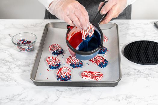 Flat lay. Dipping pretzels twists into melted chocolate to make red, white, and blue chocolate-covered pretzel twists.