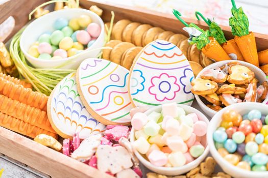 Assembling charcuterie board with Easter candies, cookies, and marshmallows.