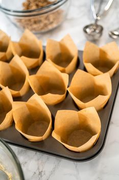 Scooping dough with dough scoop into cupcake pan lined with tulip paper muffin liners to bake banana oatmeal muffins.
