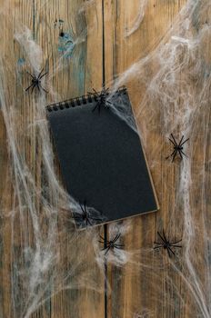 open notebook with blank black pages, spider web and black spiders on a wooden background, top view