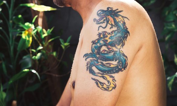 Closeup a beautiful colored dragon tattoo on the left upper arm of a man.