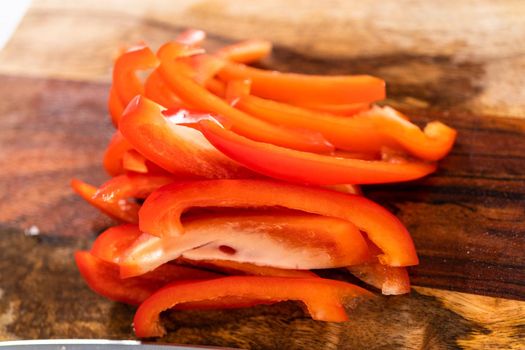 Cutting organic red bell peppers on a wood cutting board.