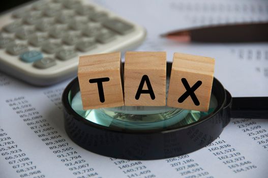 Tax word labeled wooden blocks on magnifying glass. Tax investigation concept.calculator and number analysis background. Tax concept.