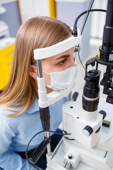 Young woman sitting in armchair looking at slit lamp during medical examination in eyes