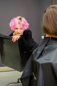 Portrait of a beautiful young caucasian woman with a new short pink hairstyle sitting in a chair at a hairdresser salon