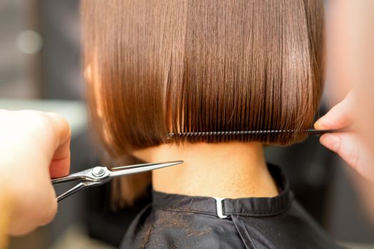 Haircut of short hair of young white woman by hands of a hairdresser in a hair salon, back view, close up