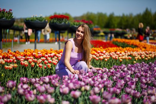 A young woman in a pink suit stands in a blooming field of tulips. Spring time