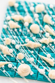 Mini mermaid chocolate bars drizzled with white chocolate, sprinkling with white pearl sugar sprinkles, and decorated with a white chocolate seashells.