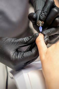 Manicure master uses electric nail file machine in a nail salon, close up