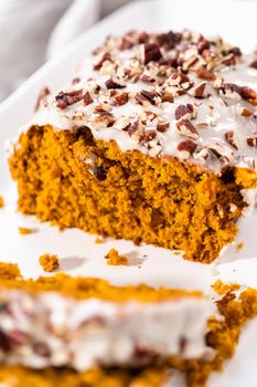 Sliced homemade pumpkin bread with a white glaze and pecans on a white serving tray.