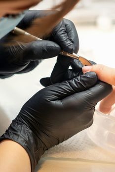 Close up professional manicurist master holding customer hand while using a cuticle pusher in a nail salon