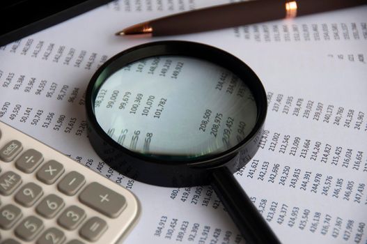 Business analysis concept - magnifying glass with pen, calculator and number analysis.