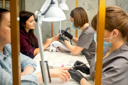 Manicure master in rubber gloves applies an electric nail file to remove the nail polish in a nail salon