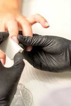 Close up of the caucasian hands of a professional manicurist are filing the nails of a young woman. Young caucasian woman receiving a manicure by a beautician with a nail file in a nail salon