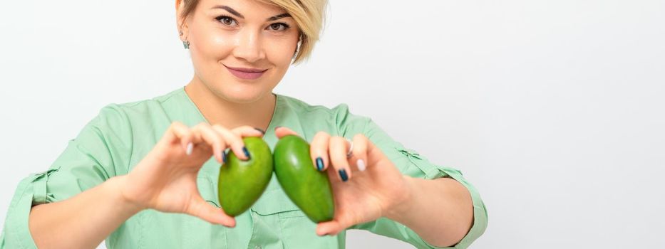 Female nutritionist doctor wearing green workwear holding green organic avocado fruit. Healthy lifestyle concept