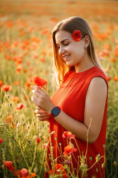 Happy blonde woman in red dress holding a flower in her hair on a poppy field. Fun summer vibes. Relaxed atmosphere, positive emotions.