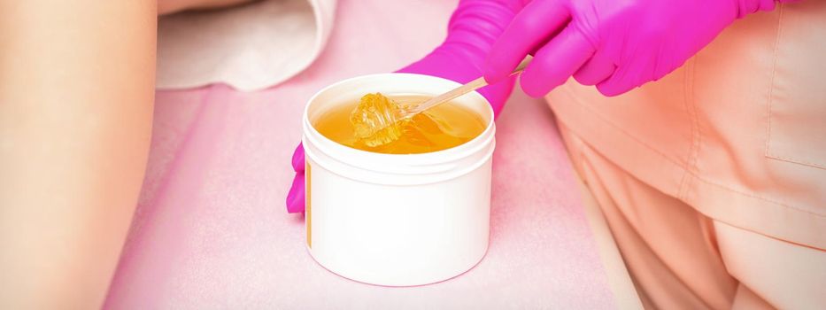Beautician with a white jar of wax sugaring before hair removal at the spa