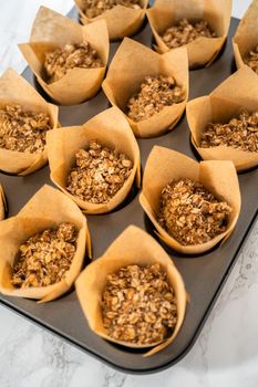 Scooping dough with dough scoop into cupcake pan lined with tulip paper muffin liners to bake banana oatmeal muffins.