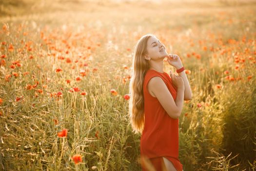 Beautiful woman in a red dress in a field of blooming poppies. Selective focus