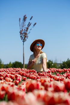 A beautiful slender woman in a hat stands in a blooming field of tulips. Spring time