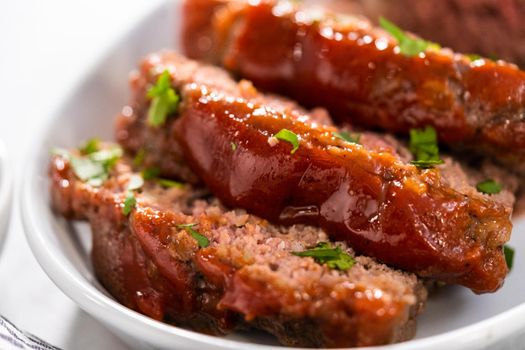 Slicing classic meatloaf with a sweet glaze on a white serving plate