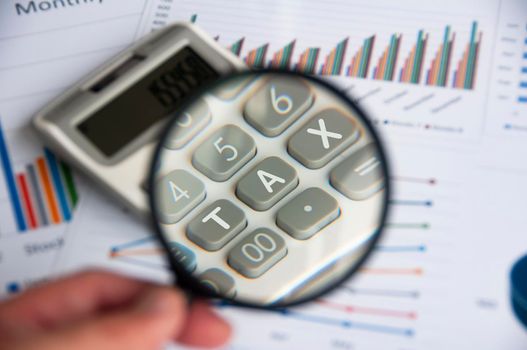 Magnifying glass focusing on TAX work on calculator. Business and tax concept