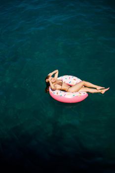 Young woman in a swimsuit swims on an inflatable ring in the sea. Summer vacation concept.