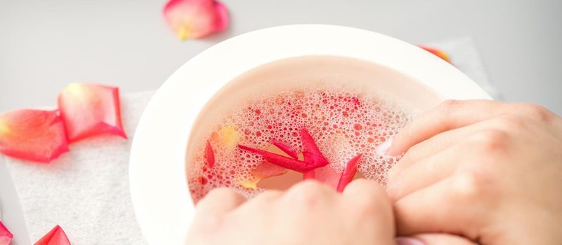 Female hands in a bowl of water with pink petals of rose flowers in spa