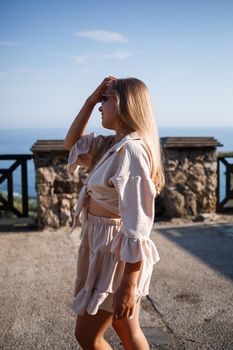 Young woman with long blond hair in a light top and skirt walks on a summer sunny day