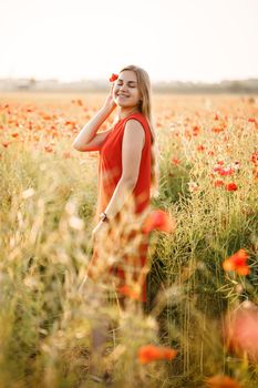 A woman of European appearance with long blonde hair and a red summer dress, she stands in a blooming poppy field