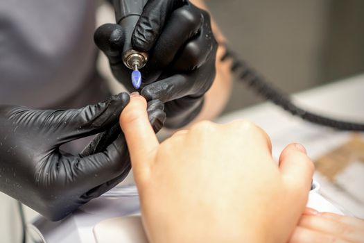 Manicure master uses electric nail file machine in a nail salon, close up