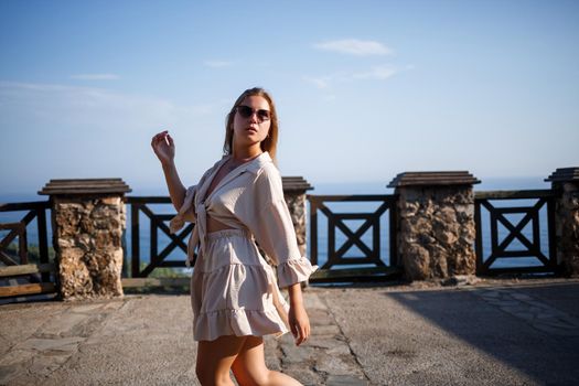 Young woman with long blond hair in a light top and skirt walks on a summer sunny day