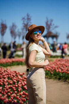 A beautiful slender woman in a hat stands in a blooming field of tulips. Spring time