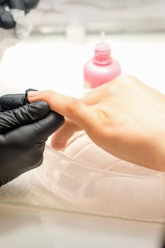 Close up professional manicure master holds the female hand of the customer and disinfects nails in a nail salon