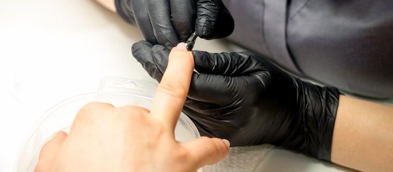 Close up professional manicurist master holding customer hand while using a cuticle pusher in a nail salon