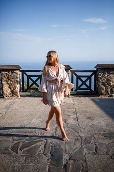 A young woman with long blond hair in a top and a skirt is walking on a summer sunny day. Happy girl with a smile on her face and in sunglasses is walking on a sunny day