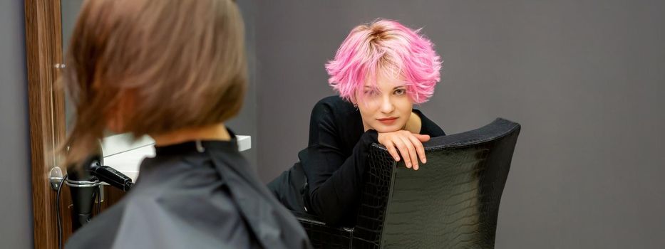 Portrait of a beautiful young caucasian woman with a new short pink hairstyle sitting in a chair at a hairdresser salon