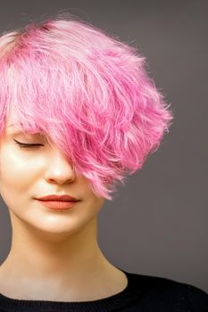 Beautiful young caucasian woman with short curly bob hairstyle dyed in pink color with closed eyes against dark gray background with copy space