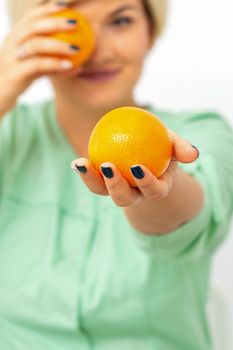 Smiling female nutritionist holding a whole orange, offering and looking at camera over white background, healthy diet concept