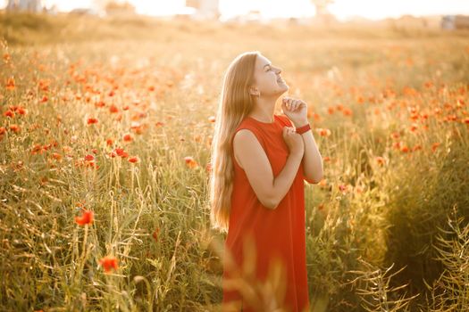 Beautiful woman in a red dress in a field of blooming poppies. Selective focus
