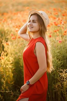 Happy cheerful woman walking on blooming field poppies. Red flowers. A blonde in a red short dress and a hat.