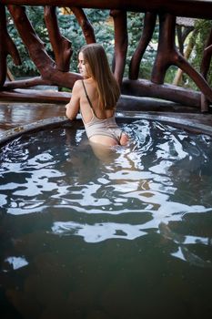 Beautiful figure woman in a swimsuit. Girl in the pool with hot water on the terrace, spa body treatments. Outdoor Jacuzzi. Jacuzzi with a girl. Relax in the open air, wellness. Cottage with spa bath