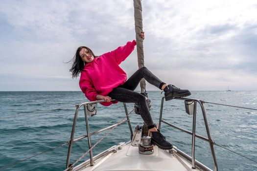 Woman standing on the nose of the yacht at a sunny summer day, breeze developing hair, beautiful sea on background.